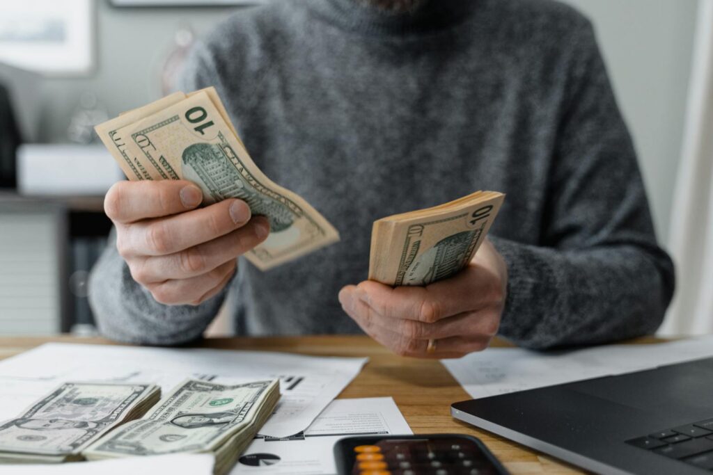 Close-up of person counting cash with a calculator and paperwork on a desk. argent qui rapport mensuellement