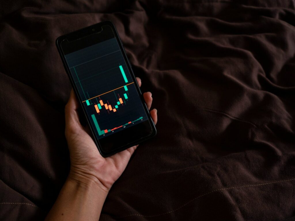 a person holding a cell phone with a chart on the screen, investir en bourse
