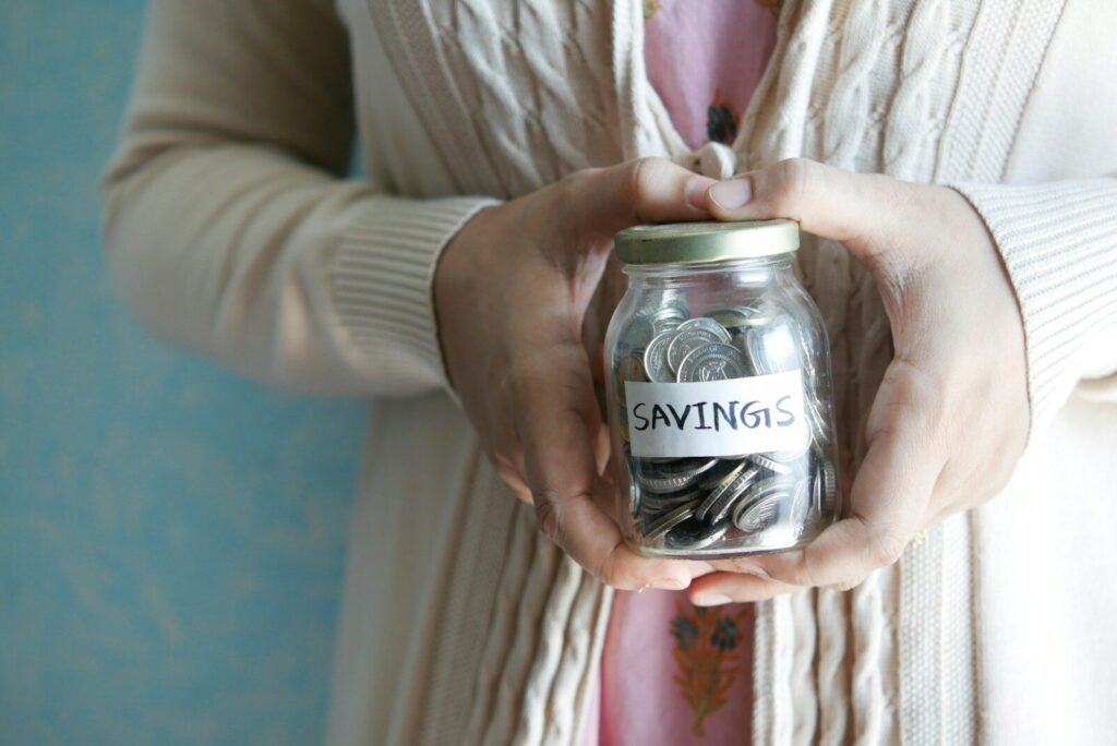a woman holding a jar with savings written on it, Combien investir en bourse pour commencer
