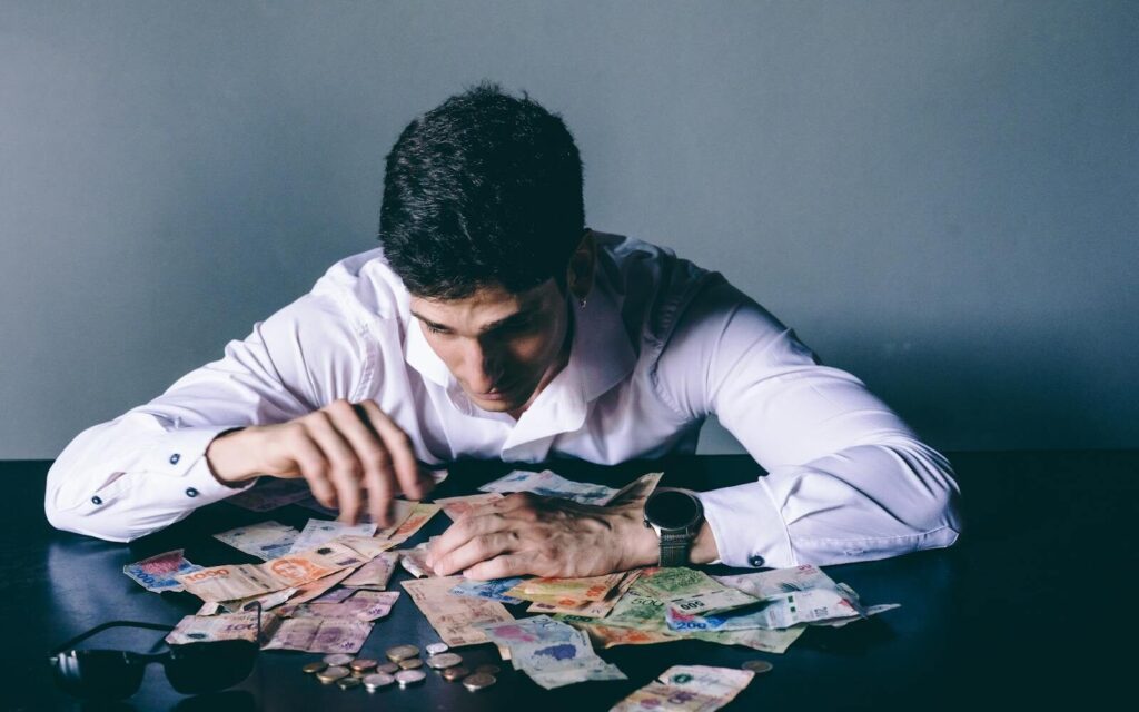 Focused man counts various international currencies on a dark desk indoors. Petrodollar