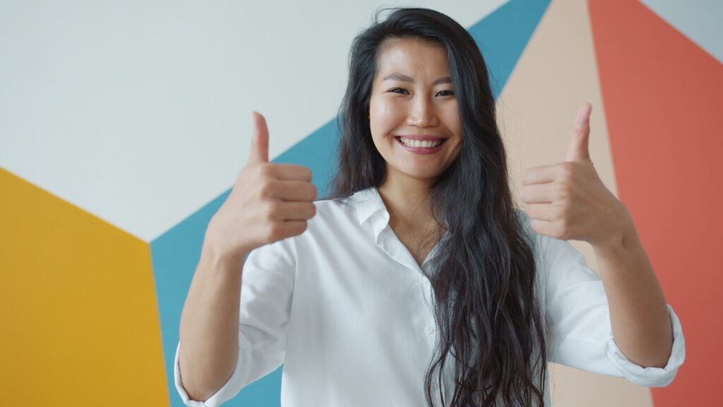 Happy woman in white shirt giving thumbs up against colorful geometric wall background.