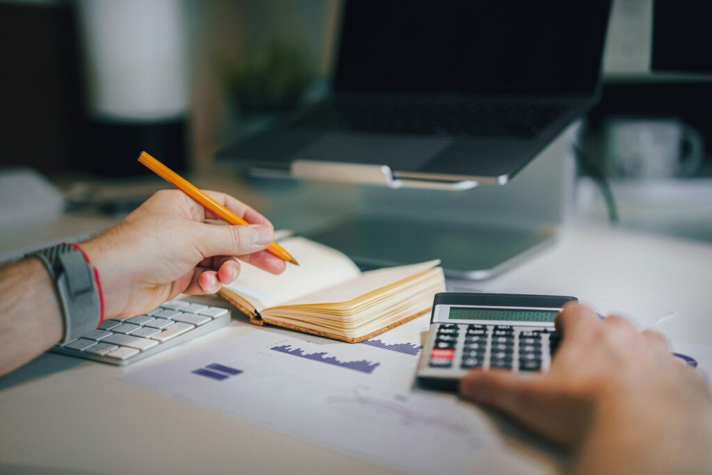 a person sitting at a desk with a calculator and a notebook, Combien mettre de côté par mois